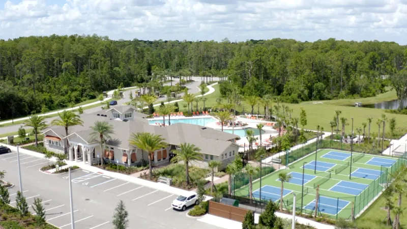 Sports courts next to clubhouse with pool and green trees in background.