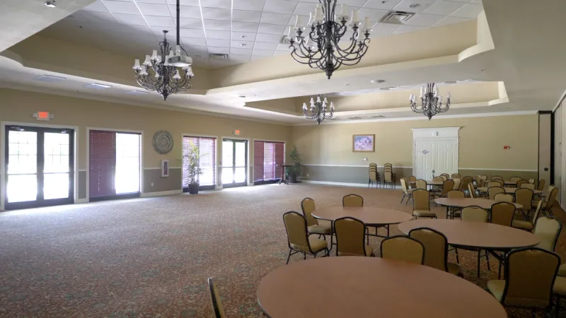 A spacious ballroom in Del Webb Southshore Falls filled with round tables and natural light streaming through large windows.