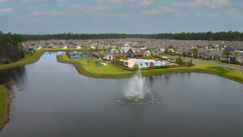 A lake with a large fountain in the middle surrounded by green lawns and the community center in the background.