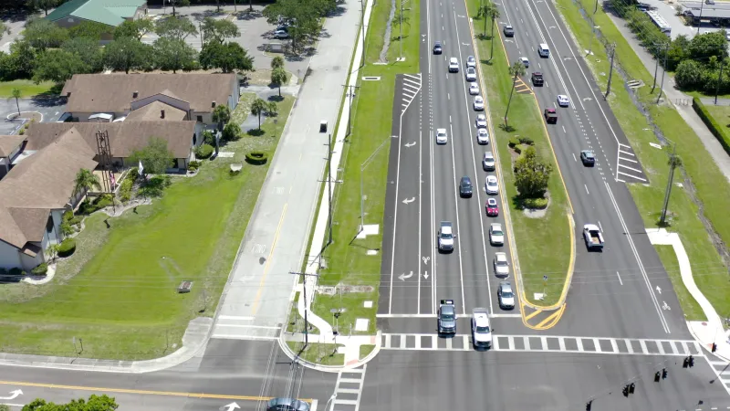 A scene roadway lined with well-manicured lawns and homes, with a golf cart path running alongside, perfect for leisurely rides through Sun City Center.