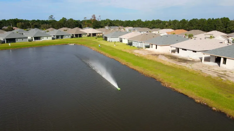 A community lake with a small RC boat racing in the distance surrounded by well manicured homes.