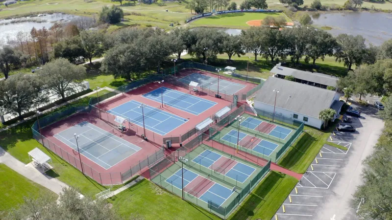 Several types of sports courts, including tennis and pickleball, surrounded by green lawns, tall trees and serene lakes at Plantation at Leesburg.