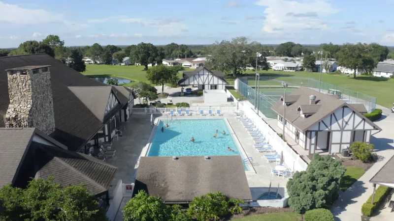 Clubhouse, pool area and sports courts with golf course and trees in background.