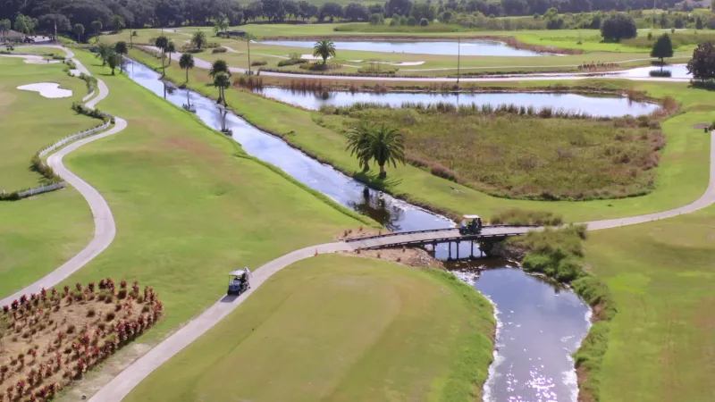 A picturesque golf course featuring numerous water features and a charming wooden bridge on the winding golf cart path.