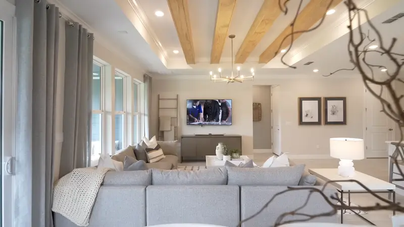 A cozy modern living room with a large sofa, a TV mounted on the wall, and natural wood accents.