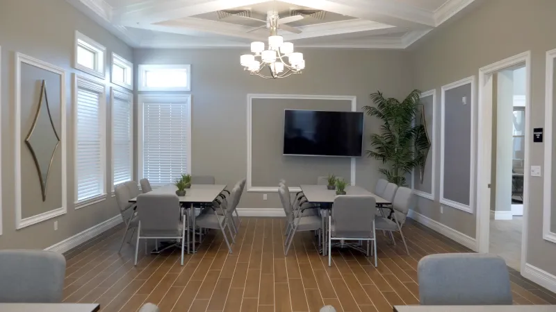 Brightly lit meeting room with tables, chairs and TV.