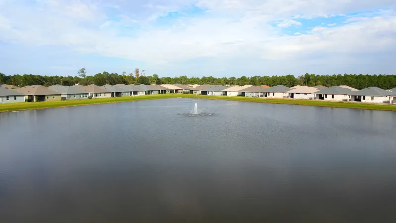 A community water feature with fountain in the center surrounded homes.