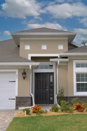 A residential home with a stucco facade and white trim with a green lawn and driveway leading up to the front door.