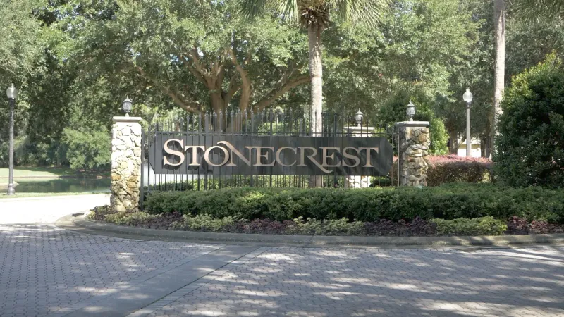 Entrance to Stonecrest, featuring a wrought-iron gate, surrounded by stone pillars and lush landscaping.