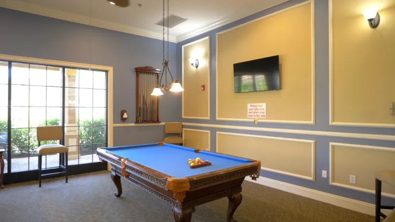 A well-lit billiard table is front a center, complemented by expansive windows in the backdrop.