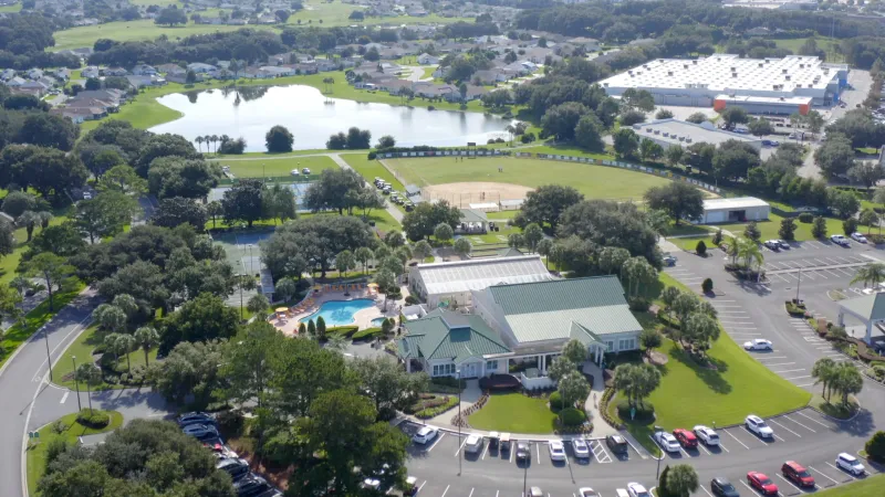 Shot of the Stonecrest clubhouse with a pool, sports facilities and a large pond surrounded by lush greenery.