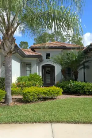 A beige, tile-roofed house at Pelican Preserve with a manicured lawn and palm trees.