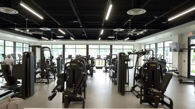 A well-equipped fitness center at Del Webb Sunbridge, featuring a variety of exercise machines and large windows for natural light.