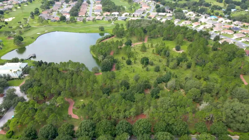Aerial view of a picturesque park featuring walking trails alongside a tranquil lake, complemented by homes in the background.