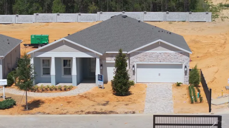 A close-up of a single-story house in Del Webb Minneola, featuring a stone facade and a two-car garage, with landscaping in progress.