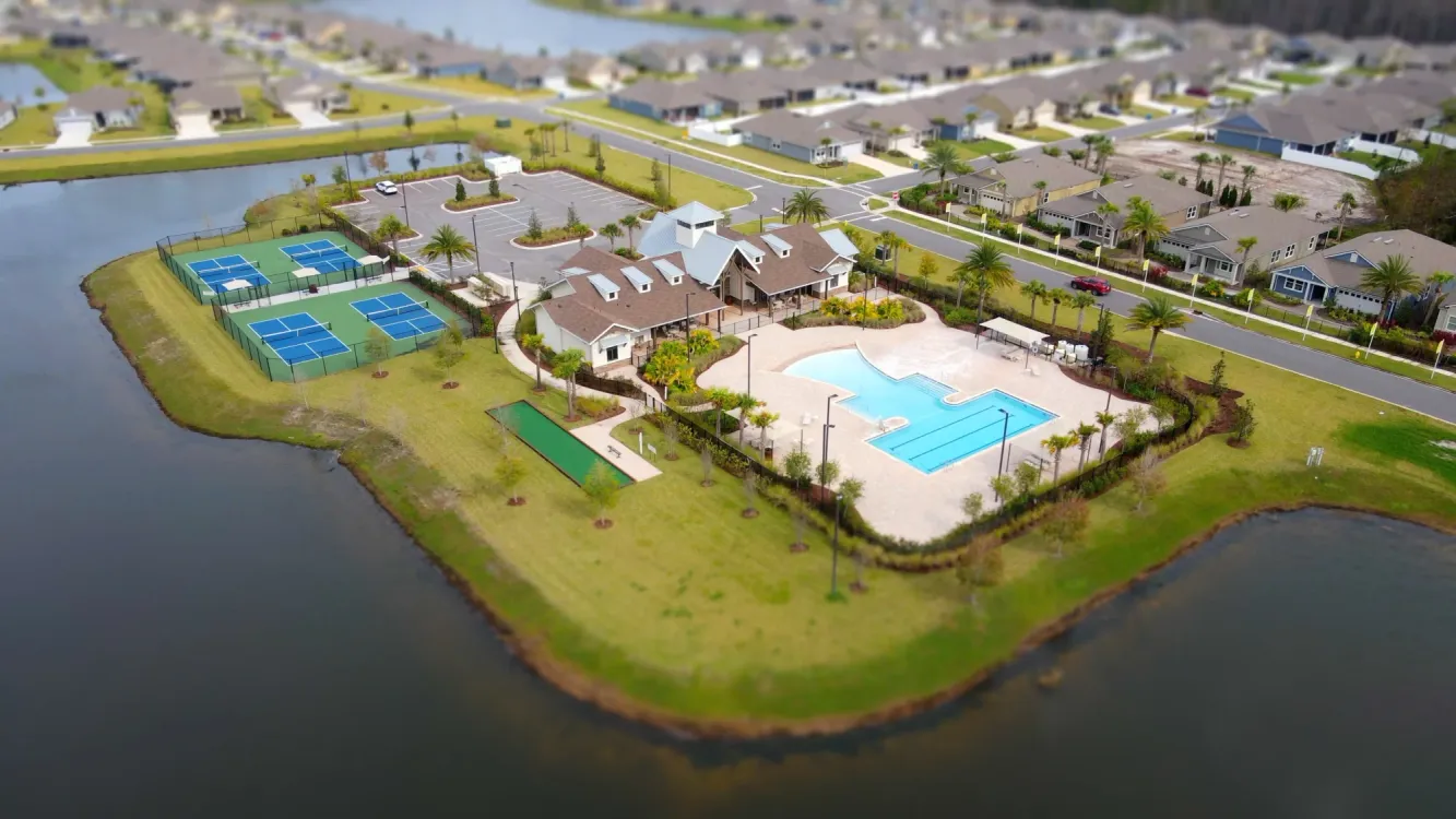 Amenities, sports courts and pool area surrounded by green area and lake.