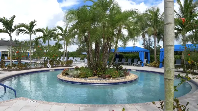 A serene pool surrounded by palm trees and blue cabanas.