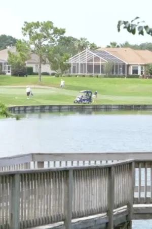Golfers swinging on a fairway with a golf cart nearby and homes in the background.