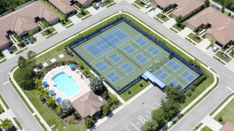 An aerial view of a pool surrounded by lounge areas with nearby tennis and pickleball courts.