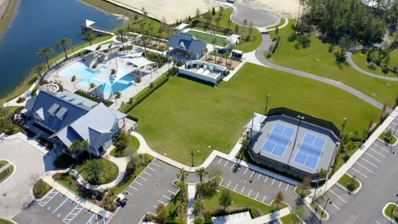 A well designed community clubhouse surrounded by a perfectly manicured lawn, sports courts and sparkling pool.