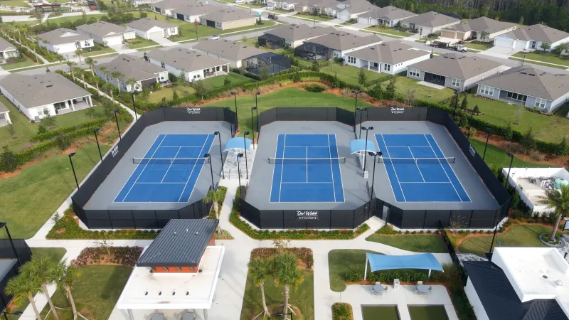 An aerial view of the Del Webb eTown sports complex showcasing blue pickleball courts, surrounded by landscaping and residential homes in the background.