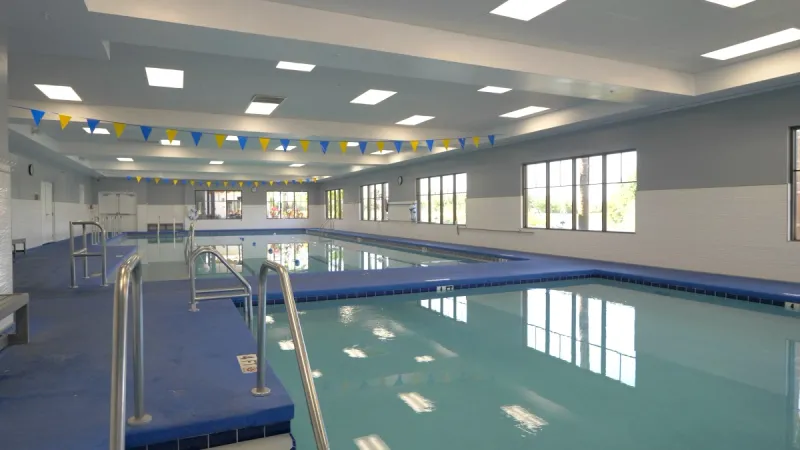 An indoor pool area with two sections, illuminated by bright lights, and adorned with small blue and yellow flags hanging overhead, creating a cheerful and inviting atmosphere.