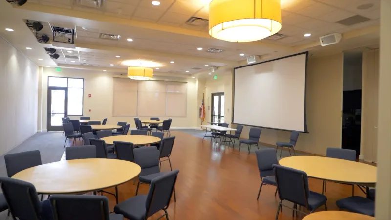 In the meeting room, round tables with chairs are set up for gatherings, accompanied by a large presentation screen.