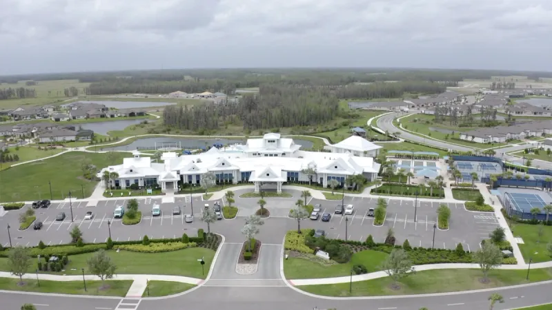 An expansive aerial view of the Del Webb Bexley clubhouse, well-maintained sports courts and a spacious parking area.