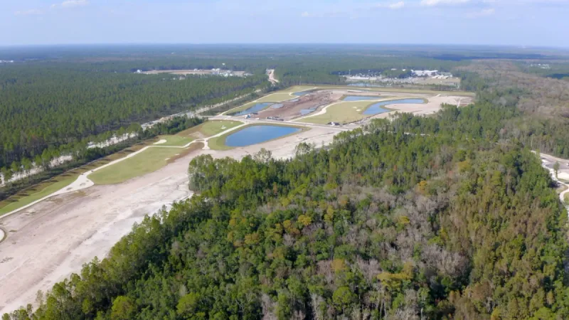 Aerial view showing Stillwater by Lennar in the distance surrounded by lush trees.