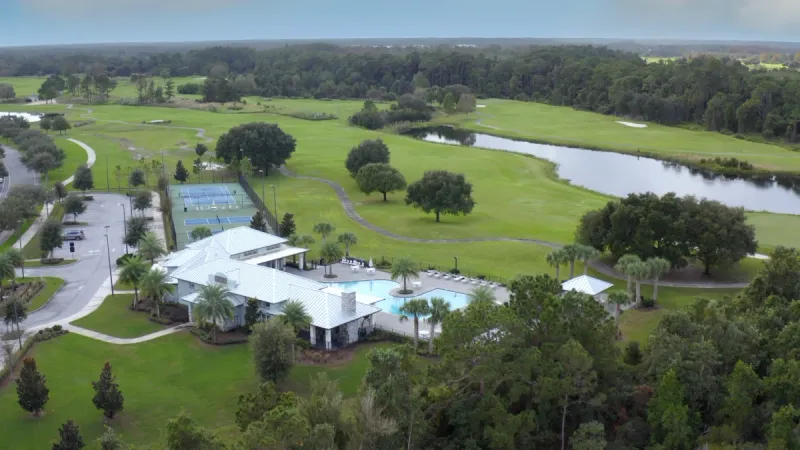 A community clubhouse and pool with tennis courts, nestled among green golf courses and waterways.