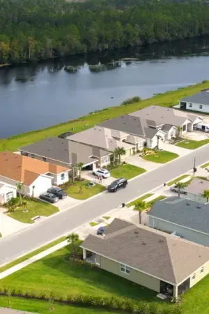 A row of houses on a residential street with manicured lawn, a lake and tall trees in the background.