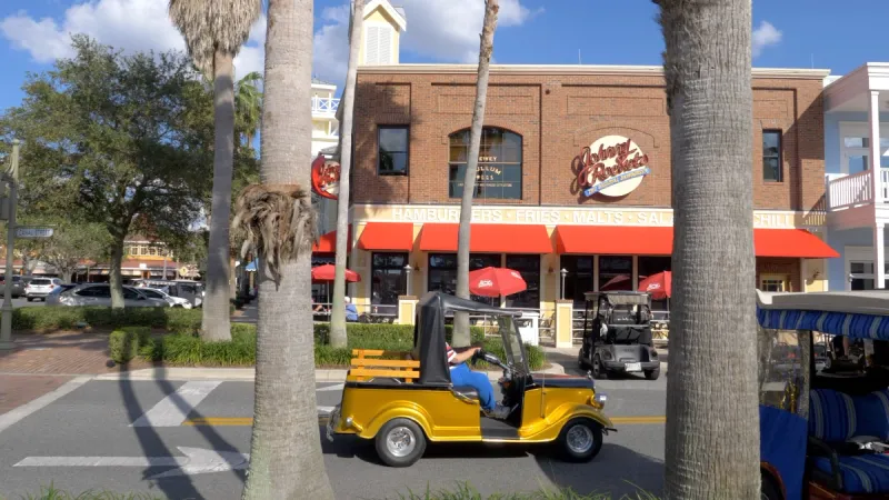 A vibrant street scene with golf carts in front of Johnny Rockets restaurant under clear blue skies.