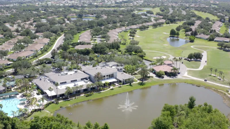 An aerial view of a Sun City Center clubhouse, surrounded by homes and a serene lake in the foreground.
