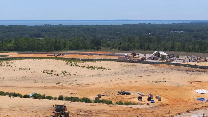 A high vantage point view of Del Webb Minneola, highlighting the sprawling construction site against a backdrop of dense greenery and distant lakes.