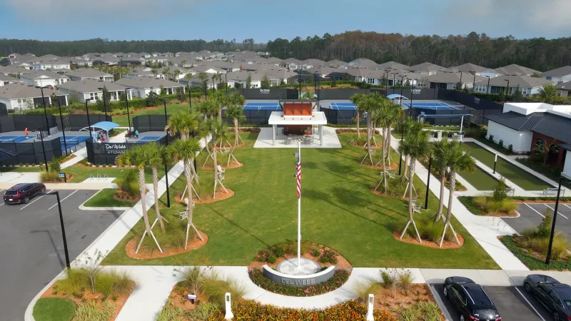 Sports courts, a central flagpole, and lush landscaping amidst residential homes.