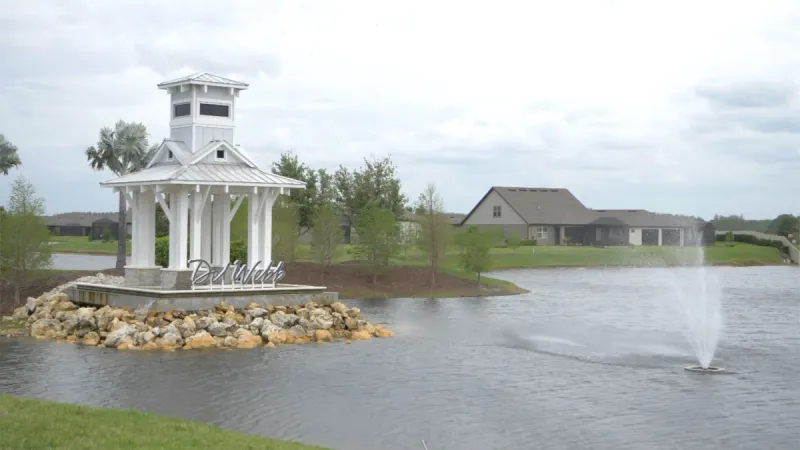 A gazebo-like structure featured in a lake with a mesmerizing fountain in the center at Del Webb Bexley.
