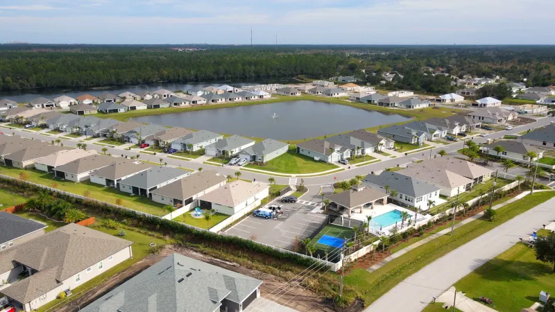 Various homes of similar style line the streets of a residential community with a water feature in the center.