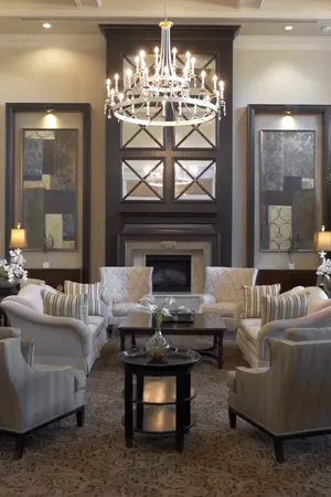 An elegant lounge area featuring plush armchairs, a central coffee table, and a grand chandelier, with decorative wall art and a fireplace.