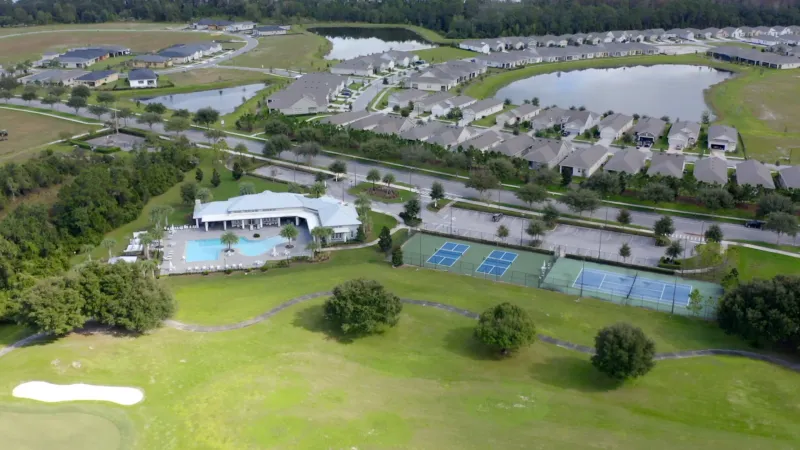 An aerial view of the Lakes at Harmony recreational areas with tennis courts, a swimming pool, and residential homes.