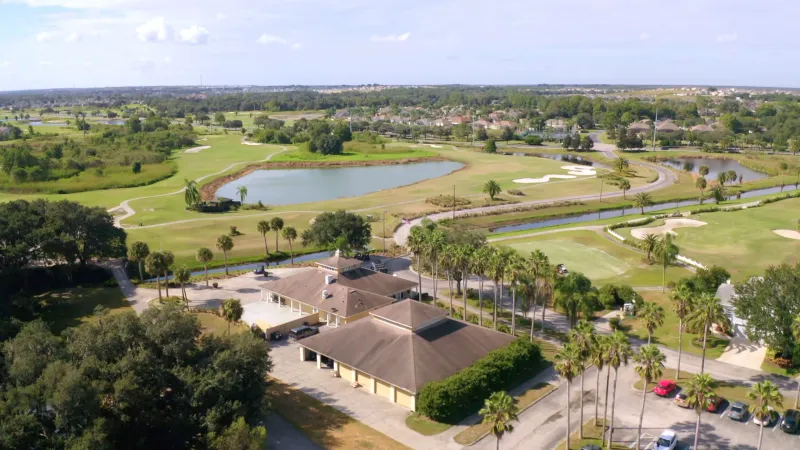 The golf club, nestled amidst lush palm trees, with a golf cart navigating a winding path adorned by scenic water features.