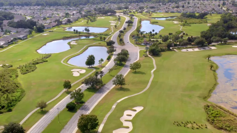 Picturesque main community roads bordered by lush golf courses on both sides, offering a view of homes in the background.