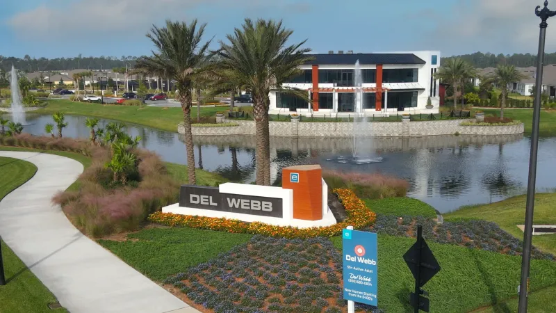 Vibrant entrance featuring the Del Webb eTown sign and moder clubhouse overlooking a serene lake.