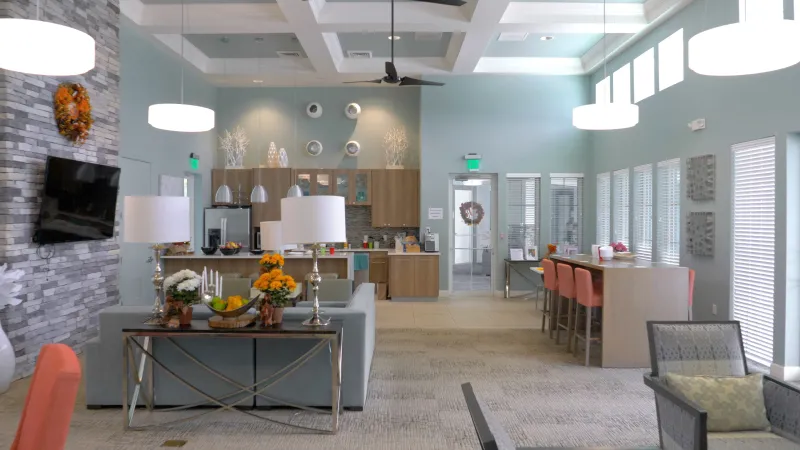 A contemporary and welcoming interior of the community clubhouse with sitting areas, a kitchenette, and decorative lighting.