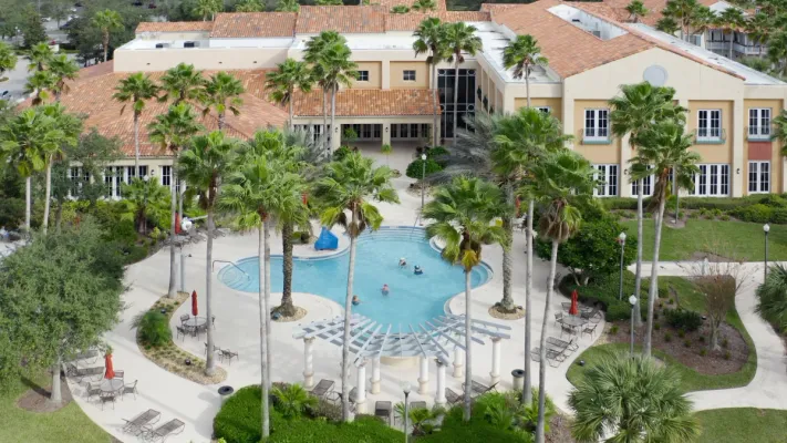 Aerial view of Solivita's community center featuring a large outdoor swimming pool surrounded by palm trees.