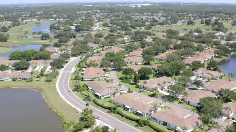 A residential road winding through a serene neighborhood, flanked by homes, lush trees, and peaceful ponds.