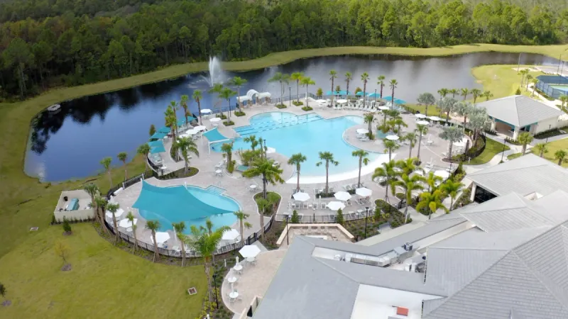 An over-view of the expansive pool and clubhouse area, flanked by a serene lake and lush greenery.