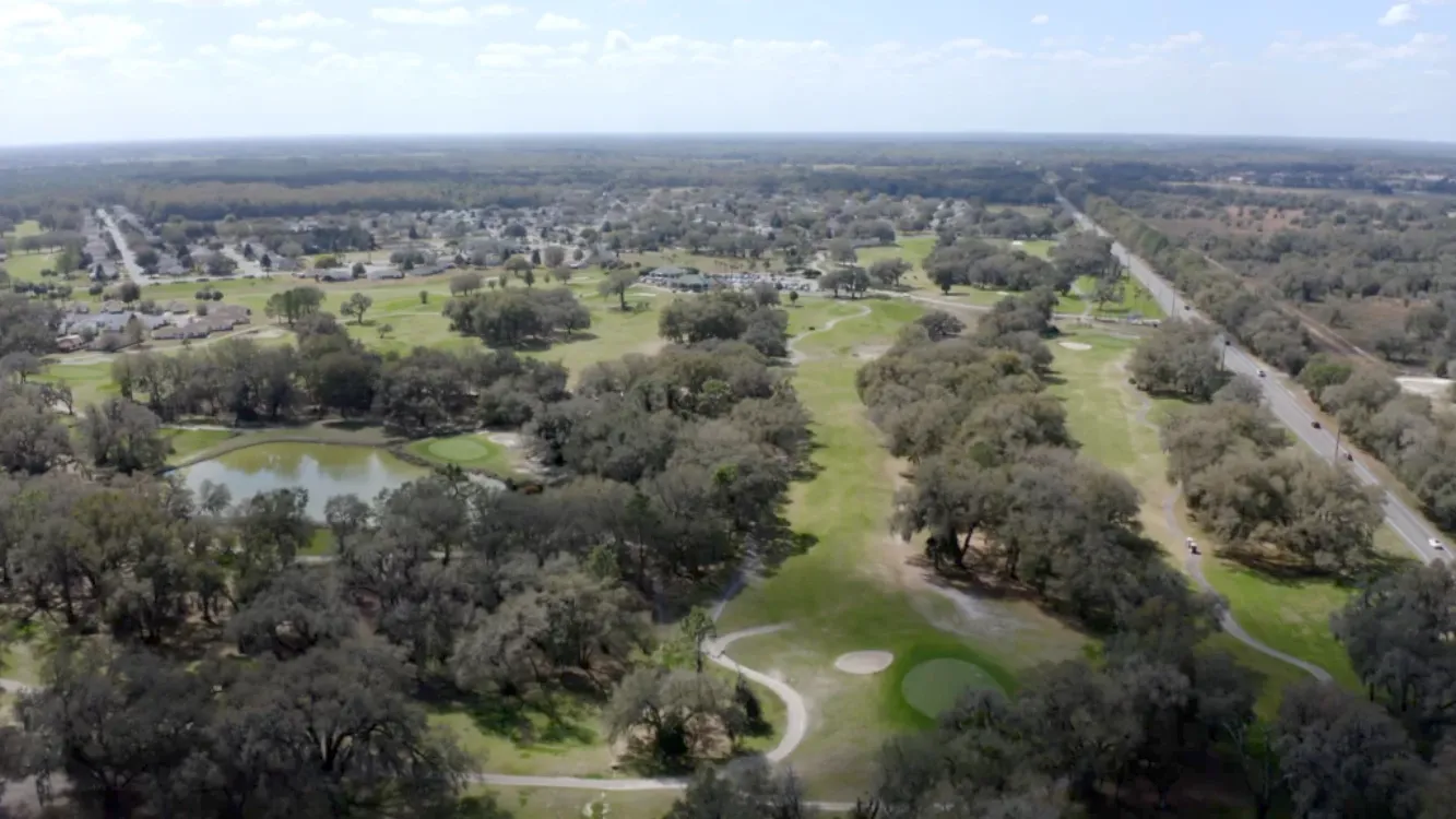 Sprawling tree lined golf course with pond and homes in background