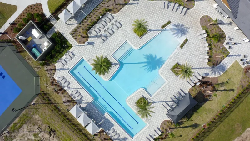 Birdseye view of a pristine pool with plenty of lounge chairs, surrounded by beautiful landscaping.