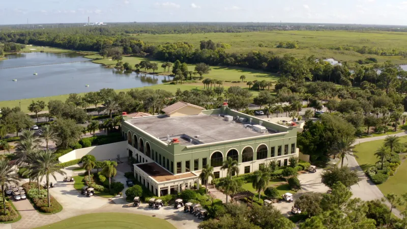An aerial view of a grand clubhouse at Pelican Preserve with lush surroundings and a lake.