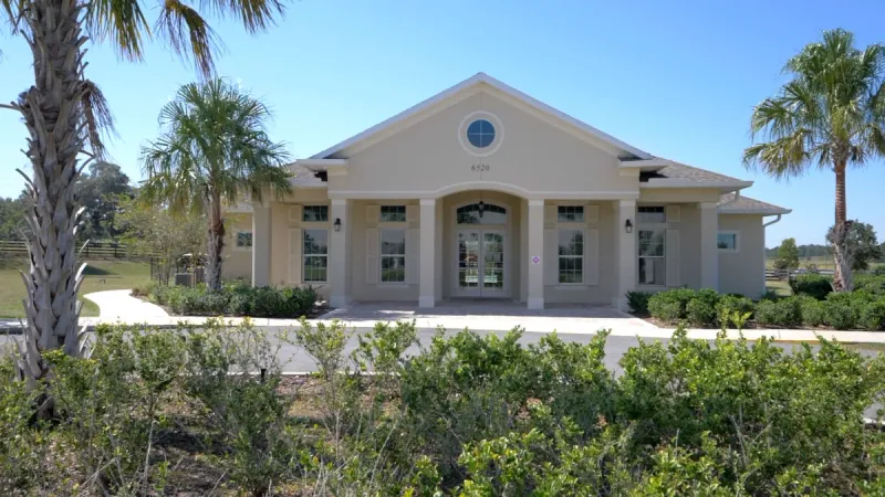The front of the JB Ranch clubhouse with landscaping in the foreground and palm trees in the background.